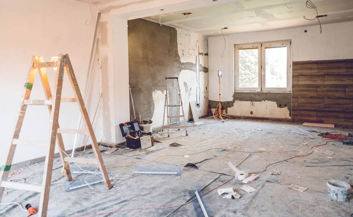 Kambarys renovuojamas – sienos šviežiai tinkuotos, grindis dengia apsauginė plėvelė, yra kopėčios ir dėžės su įrankiais. 