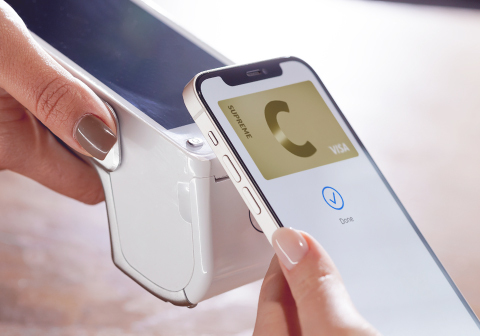 A smartphone over a contactless payment terminal, paying with a C supreme card.