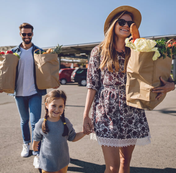 Smiling family after shopping — mother, daughter, and father holding grocery bags.